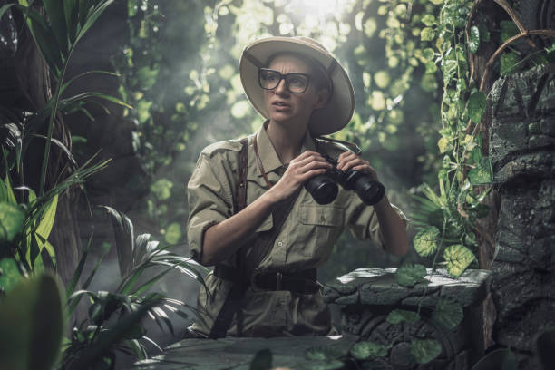 Brave woman exploring the tropical jungle and finding ancient ruins, she is holding binoculars and looking around