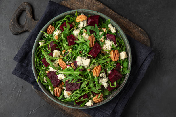istock Beet or beetroot salad with fresh arugula, blue cheese and pecan nuts in a plate on black background. top view 1313241809