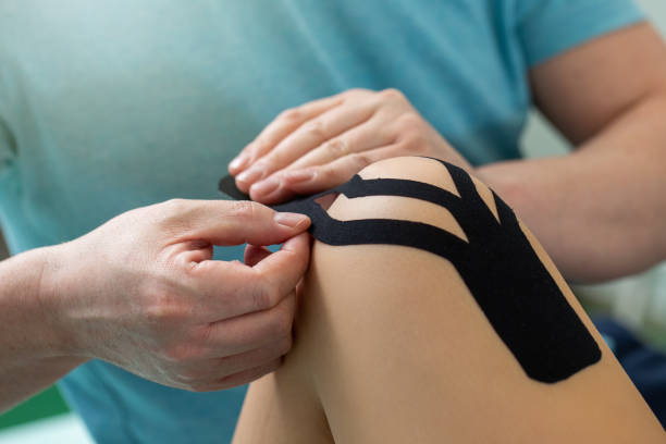 Physiotherapist applying kinesiology tape to patient knee. Physiotherapist applying kinesiology tape to patient knee. Therapist treating female Caucasian athlete with a functional bandage. Post traumatic rehabilitation and sport physical therapy. sports medicine photos stock pictures, royalty-free photos & images