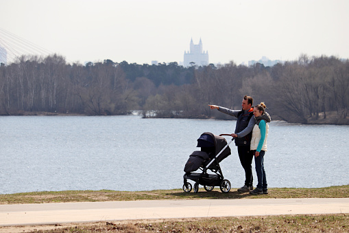 Moscow, Russia - April 2021: Couple with baby pram standing on Moscow river background in Moscow