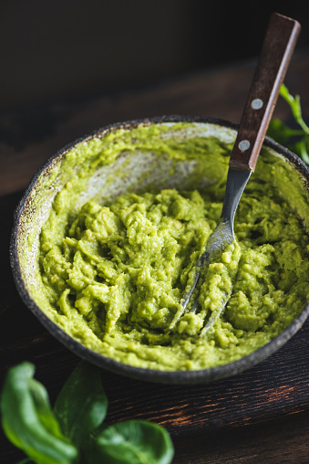 Mashed avocado sauce in a bowl on dark wooden table background