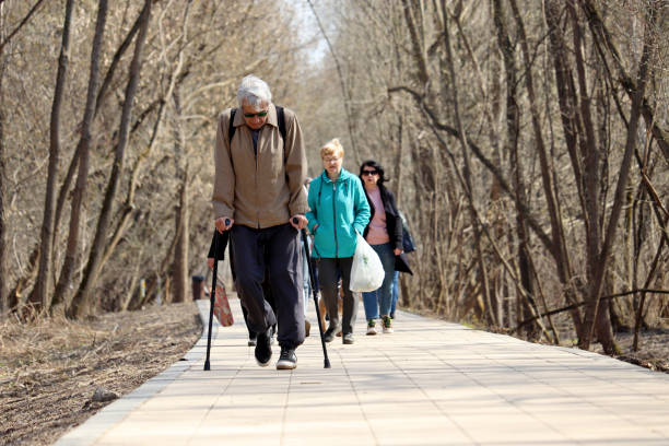 Moscow, Russia - April 2021: Elderly man walking with a sticks on a street on people background in Moscow. Limping, diseases of the spine