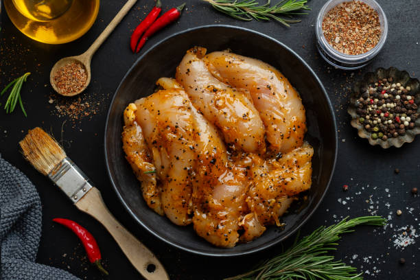 pechuga de pollo marinada cruda sobre fondo oscuro con especias listas para cocinar. - marinated fotografías e imágenes de stock