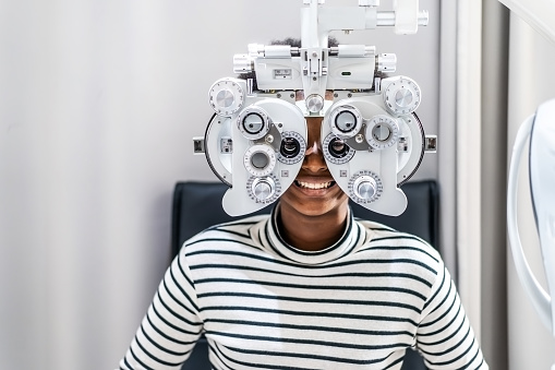 Smiling young woman african american afro hair doing Eye test on optical phoropter, checking on her eye with optometry machine