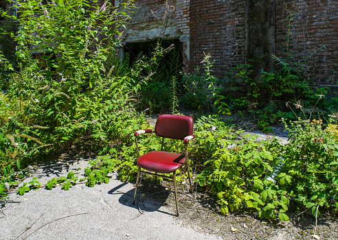 Old red chair surrounded by weed in abandoned factory