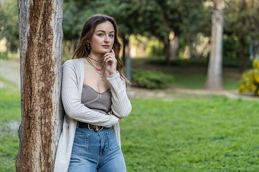 Portrait of a pretty young Caucasian woman leaning against a tree