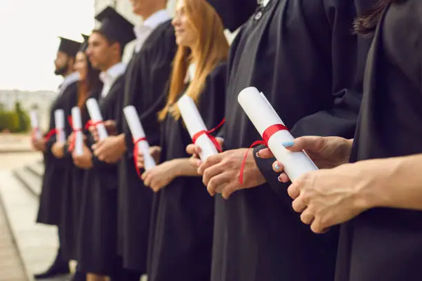 Photo of Graduate concept.Cropped image of row of students in black robes with diplomas in hands at graduation ceremony