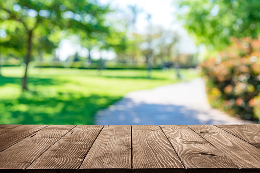 Empty rustic wooden table with defocused park footpath and green lush foliage at background. Ideal for product display on top of the table. Predominant color are green and brown. XXXL 63Mp outdoors photo taken with SONY A7rII and Zeiss Batis 40mm F2.0 CF