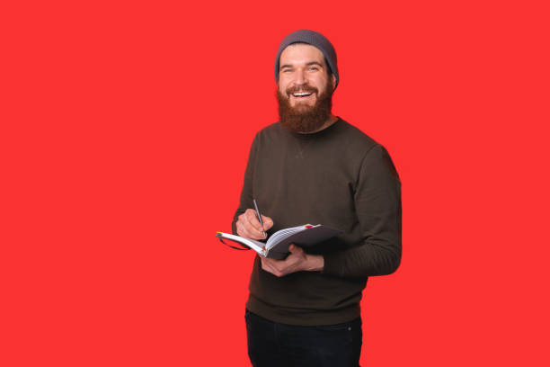 istock Happy bearded hipster man writing in planner over red background 1313258829