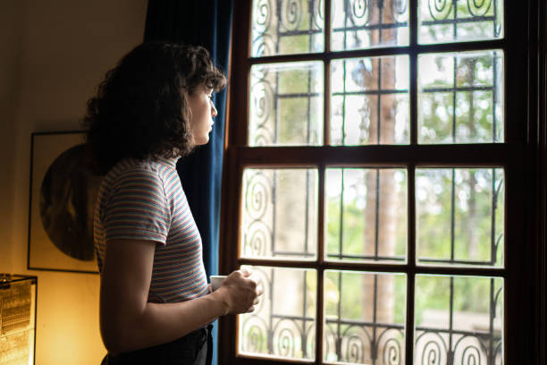 istock Transgender woman drinking tea looking through the window at home 1313261773