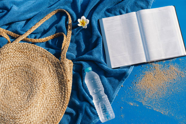 istock Summer vacation still life. Straw bag, blue towel, fresh water and open book. 1313262543