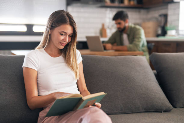 lovely brunette sitting on couch, reading a book - working at home domestic kitchen laptop contemporary imagens e fotografias de stock