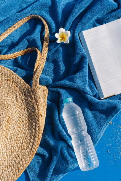 istock Summer vacation still life. Straw bag, blue towel, fresh water and open book. 1313262737