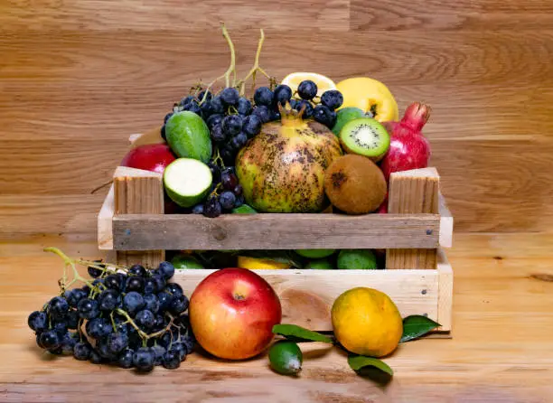 Assortment of fruits in wooden box, on wooden background. The concept of healthy food. pomegranate, grapes, kiwi, and mandarin