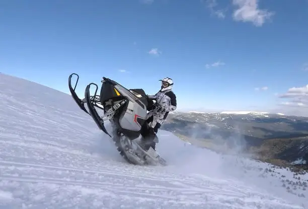 RAIDER JUMPING WITH A POWERFUL SNOWMOBILE ON A SNOWY HILLSIDE