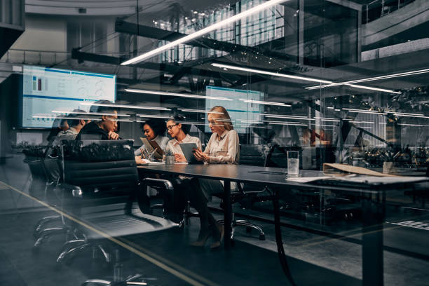 des affaires modernes. jeunes femmes et hommes d’affaires sérieux concentrés travaillant dans une salle de conférence travaillant sur une présentation de projet. la lumière d’un bureau spacieux se reflète à travers le verre. - business office business person window photos et images de collection