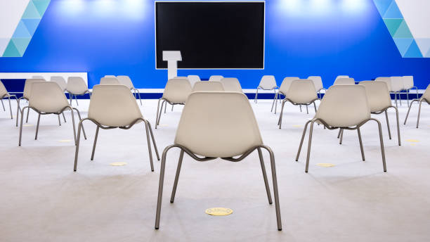 istock Super conference hall with white chairs and colored illumination and blank screen, social distance 1313265648