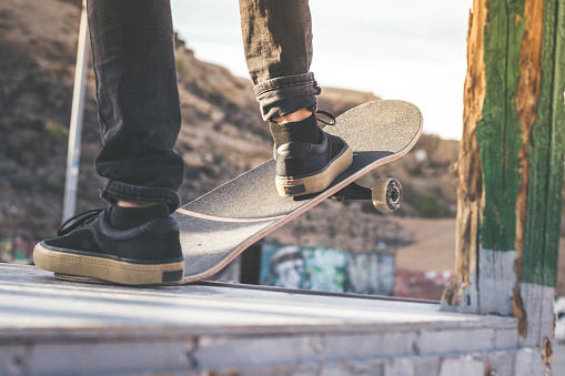 Close up view of teen's feet on a skateboard ready to start a ride over the half pipe. Skater starting jumps and tricks at the skate park. Let's go enjoying. Youth, future brave, danger, risk concept