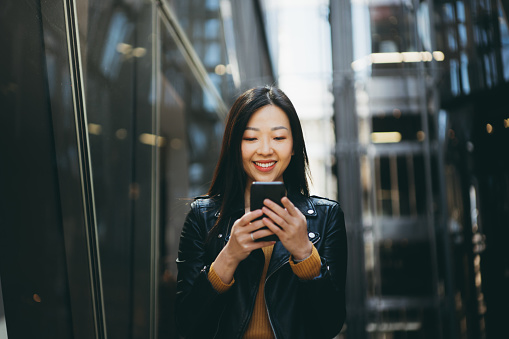 Asian cheerful woman using smartphone on the street.