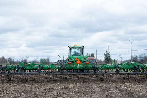 Uxbridge, ON, Canada - April 17, 2021:  A John Deere tractor and disc harrow in farm filed, to get the land ready for corn crops.