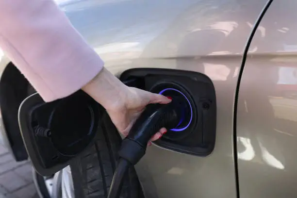 Woman hand holding charger for car closeup. Ecological fuel concept