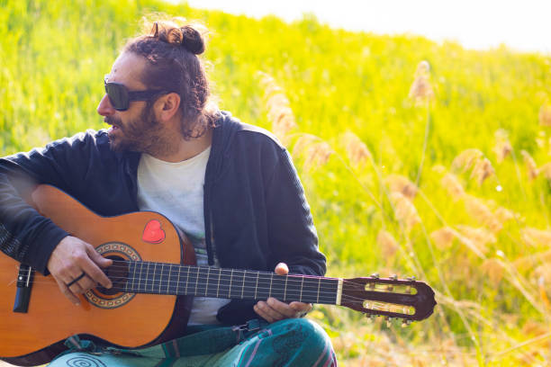 istock Hippy man with beard and glasses playing guitar outdoors on the grass 1313277117