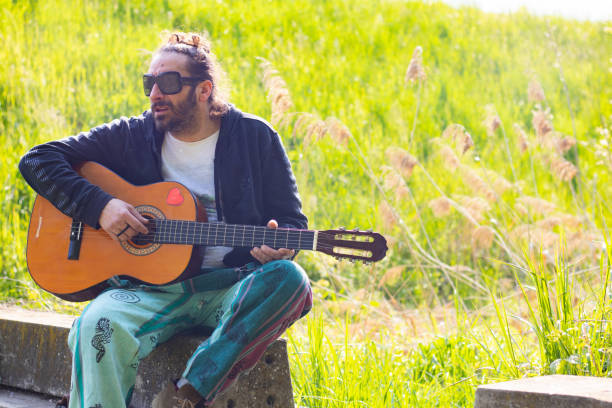 istock Hippy man with beard and glasses playing guitar outdoors on the grass 1313279826