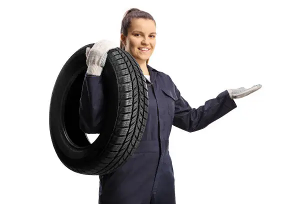 Female auto mechanic carrying a tire on her shoulder isolated on white background