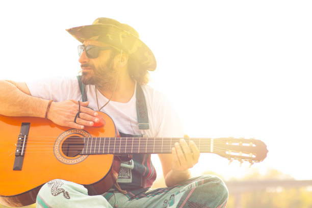 istock Hippy man with hat beard and glasses playing guitar outdoors on the beach 1313281602