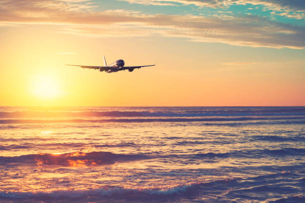istock Airplane flying over tropical beach with smooth wave and sunset sky abstract background. 1313282977