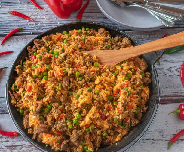 Spicy and tasty minced meat dish with greek vegetable rice served in a rustic cast iron pan on wooden table background from above
