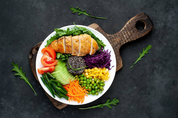 istock Bowl Buddha . Quinoa, chicken breast, arugula, avocado, red cabbage, carrot, green peas, corn, tomato, green beans in a white plate on a stone background. 1313287219