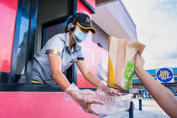 el personal femenino de mcdonald's entrega comida a los clientes a través de la puerta del coche en el punto de recogida en bangkok, tailandia - drive in restaurant fotografías e imágenes de stock