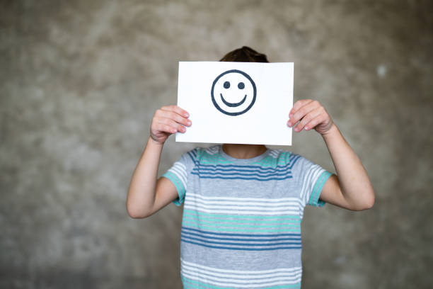 niño sosteniendo un dibujo de cara de sonrisa. emoción feliz. - smiley face smiling sign people fotografías e imágenes de stock