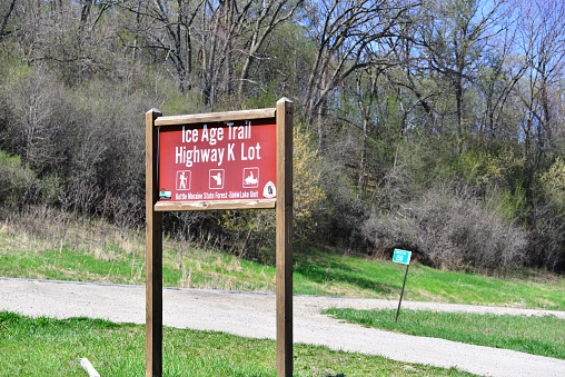 Hartland, Wisconsin - USA - Loew Lake Ice Age Trail Parking Lot sign on an beautiful spring day washed in sunlight with budding trees beyond in the Kettle Moraine State Forest Area.