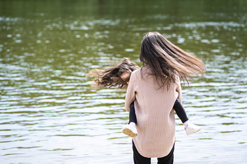 Happy woman and little girl playing together outside on scenic spring sandy beach.  Happy white family of young mom and daughter enjoying warm spring nature outside