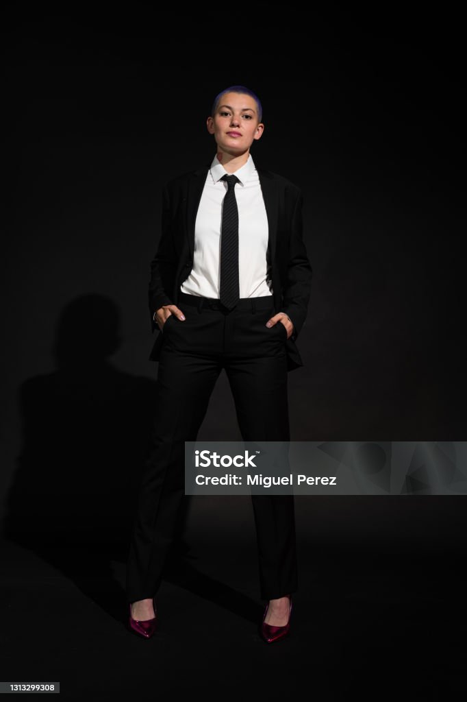 Young Citizen in Black Suit, Tie and High Heels A young citizen wearing a black suit, black tie and colorful high heeled shoes poses before a dark background 25-29 Years Stock Photo