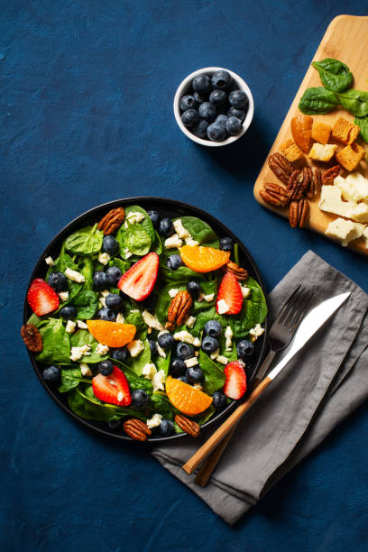 Summer salad with berries, cheese and spinach on blue background