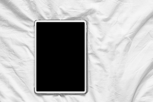 Top view mockup of white tablet pc with blank desktop white screen on a cozy white bed at home