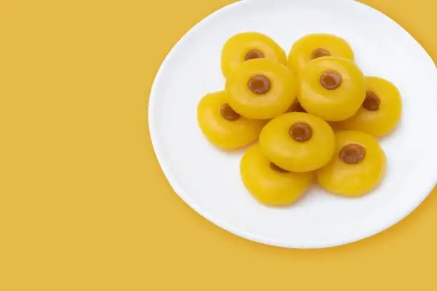 Kanom Sanay Chan, traditional sweet dessert originating in Thailand - Nutmeg –like yellow sweetmeats, serving on white plate isolated on yellow