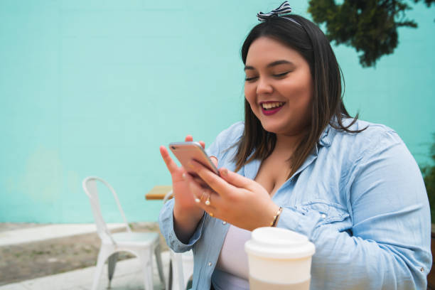 istock Young plus size woman using phone at coffee shop. 1313302099
