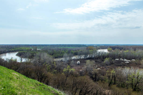 istock Panoramic view from the high bank to the river, forest, green meadow and beautiful fields. View from the high bank to the spring river and the trees around. 1313303696