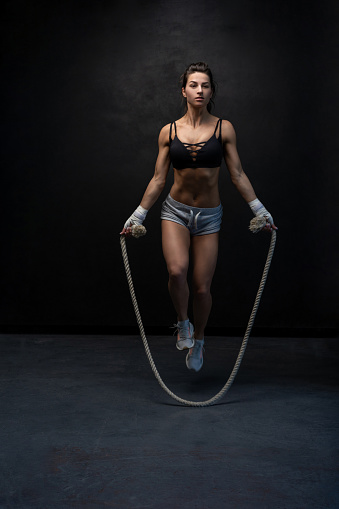 Studio shot of fit and muscular woman with jumping rope standing on black background. Sports and fitness concept.