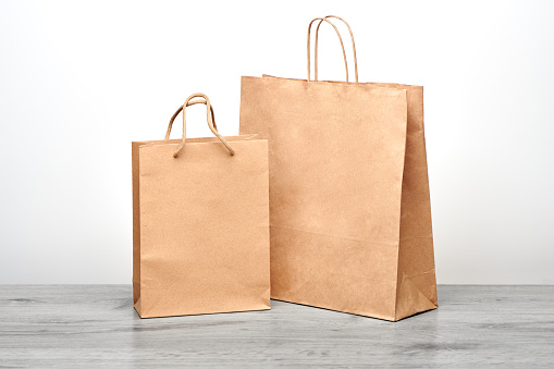 Small and big paper bag with handles isolated. Kraft paper bag mockup on wooden table. Recycled shopping bag for product or food home delivery.