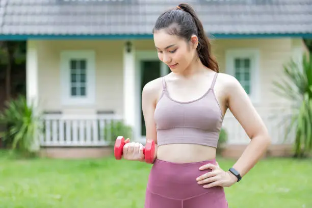 Female fitness instructor exercising with small dumbbell on frontyard.