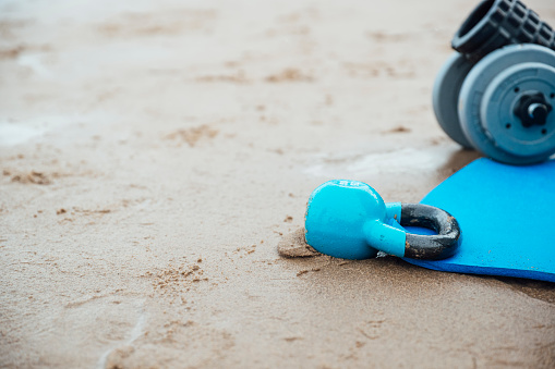 Close-up shot of a variety of workout equipment laid out on a blue exercise mat before a workout on the beach.