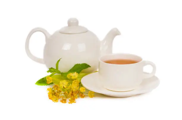 herbal linden tea in white porcelain cup and teapot on white background