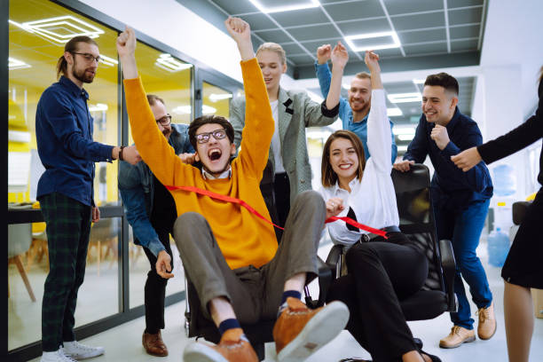 istock Friendly work team  ride chairs in office room cheerfully excited diverse employees laugh while enjoying fun work break activities, creative friendly workers play a game together. 1313318155