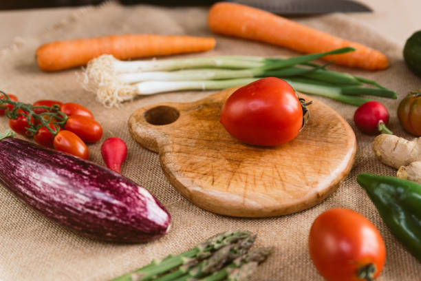 istock wood chopping board with tomato rounded by springtime fresh vegetables like eggplant and carrots on rustic fabric. concept of spring food and organic vegan nutrition 1313318349