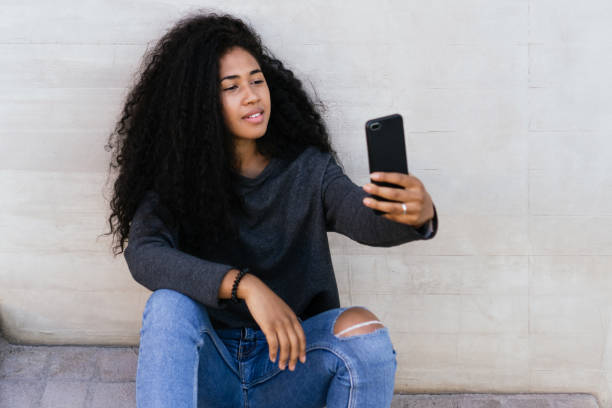 istock young afro girl using her smart phone sitting outside. 1313318821